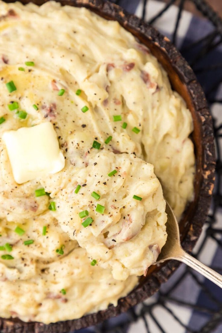 a bowl filled with mashed potatoes topped with butter and green onions next to a spoon