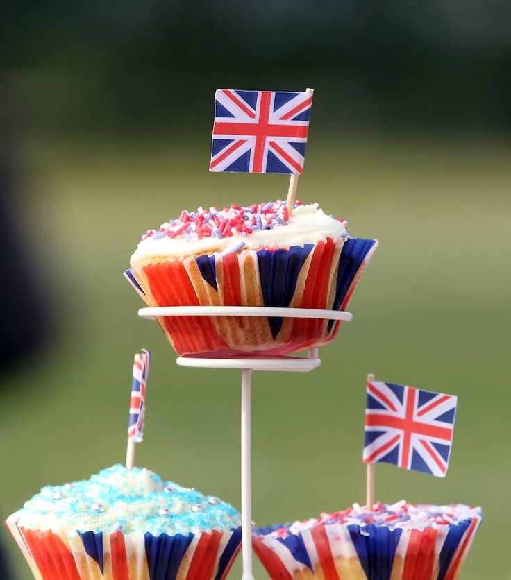 cupcakes decorated with british flags are displayed on a cake stand in front of a blurry background