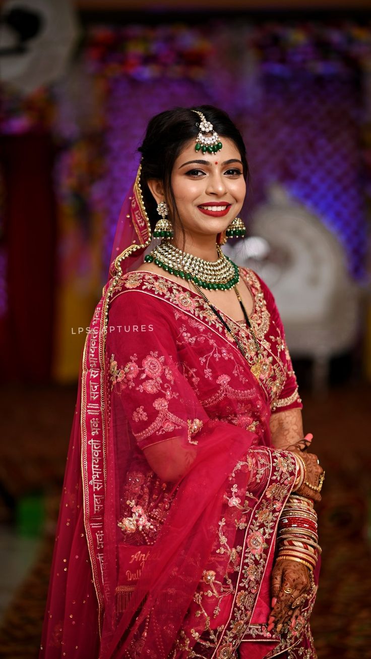 a woman in a red and gold bridal outfit with jewelry on her head, smiling at the camera