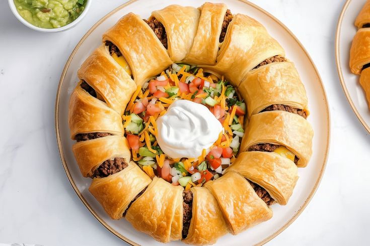 a white plate topped with pastries covered in cheese and veggies next to a bowl of guacamole