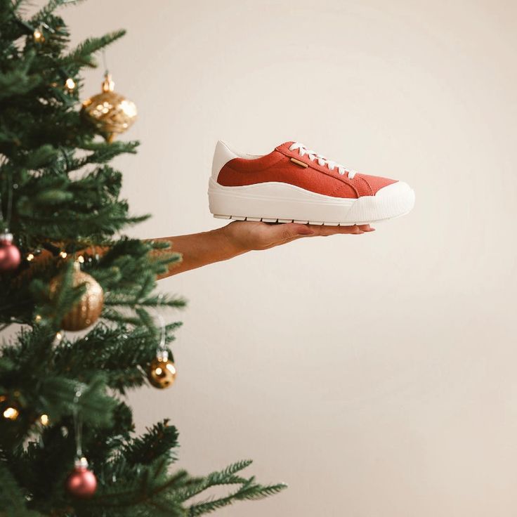 a person holding up a red shoe in front of a christmas tree with gold ornaments