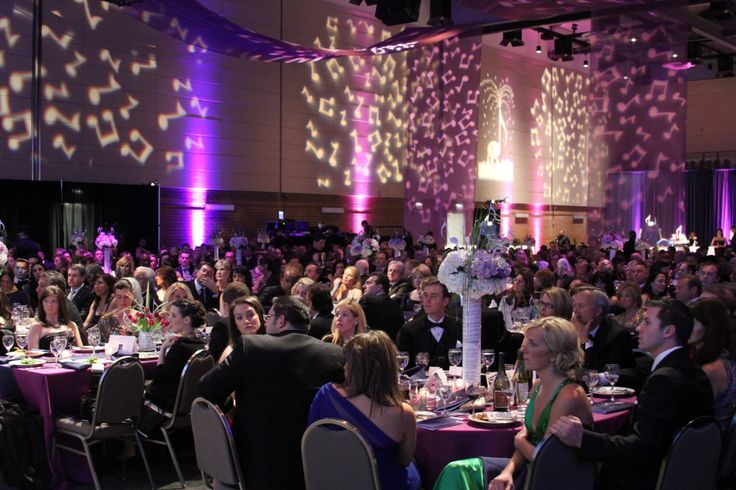 a large group of people sitting at tables in a room with purple lighting on the walls