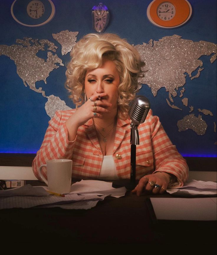 a woman sitting at a table with a microphone in front of her and a world map on the wall behind her