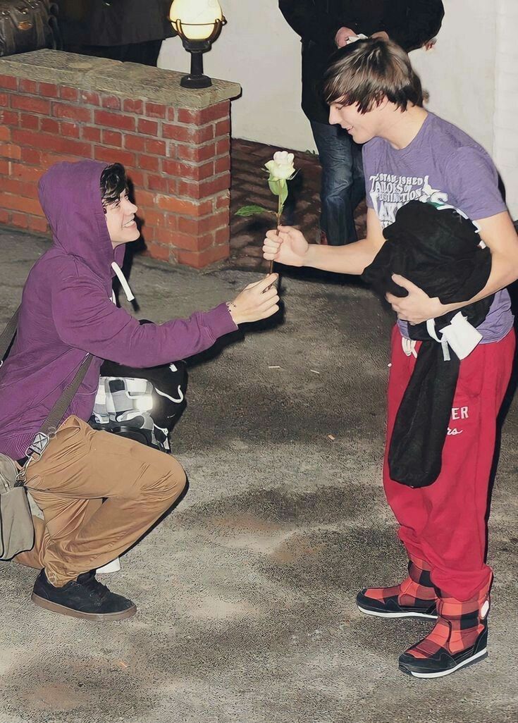 two boys in purple shirts and red pants are playing with each other while one boy is holding a rose