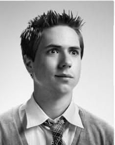 a black and white photo of a young man wearing a sweater, tie and vest