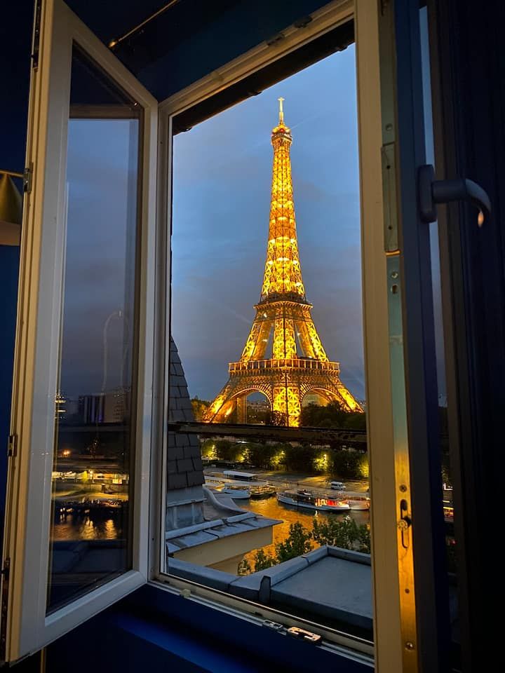 the eiffel tower lit up at night seen through an open window in a building