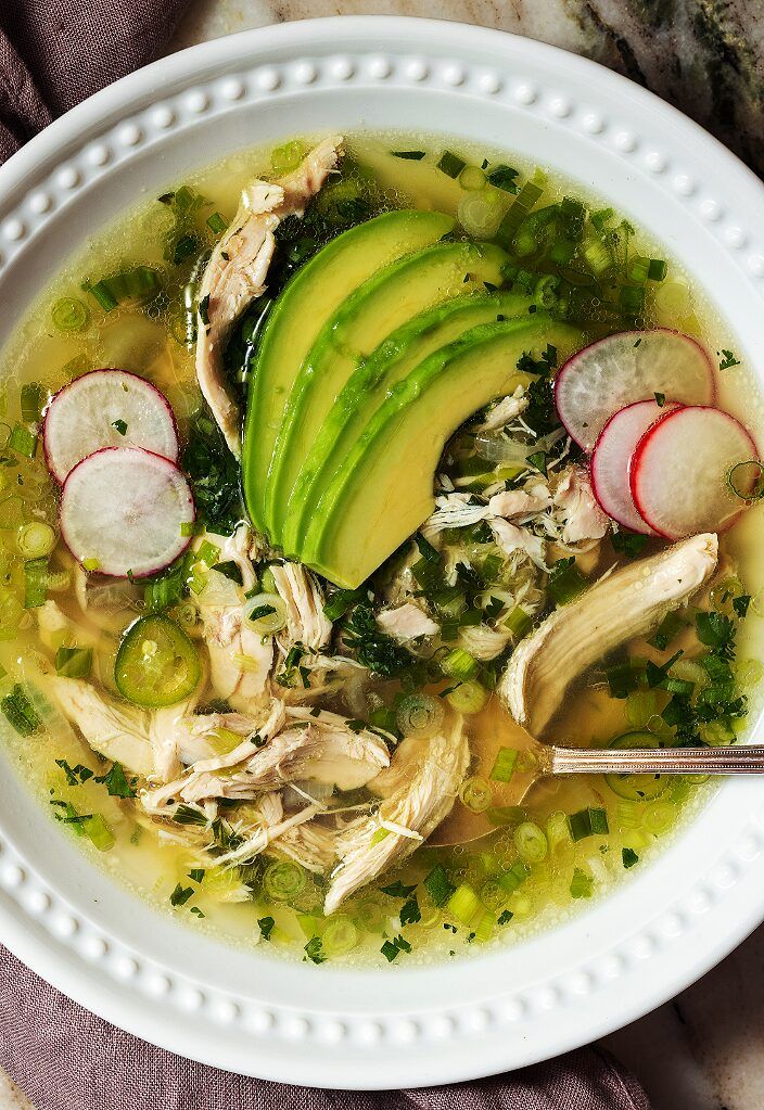 a white bowl filled with chicken, avocado and sliced radishes