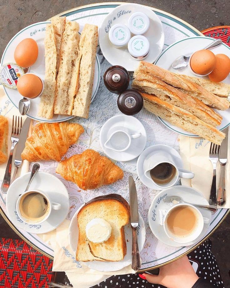 a table topped with lots of breakfast foods and cups of coffee next to each other