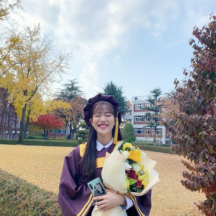 a woman dressed in graduation clothes holding flowers