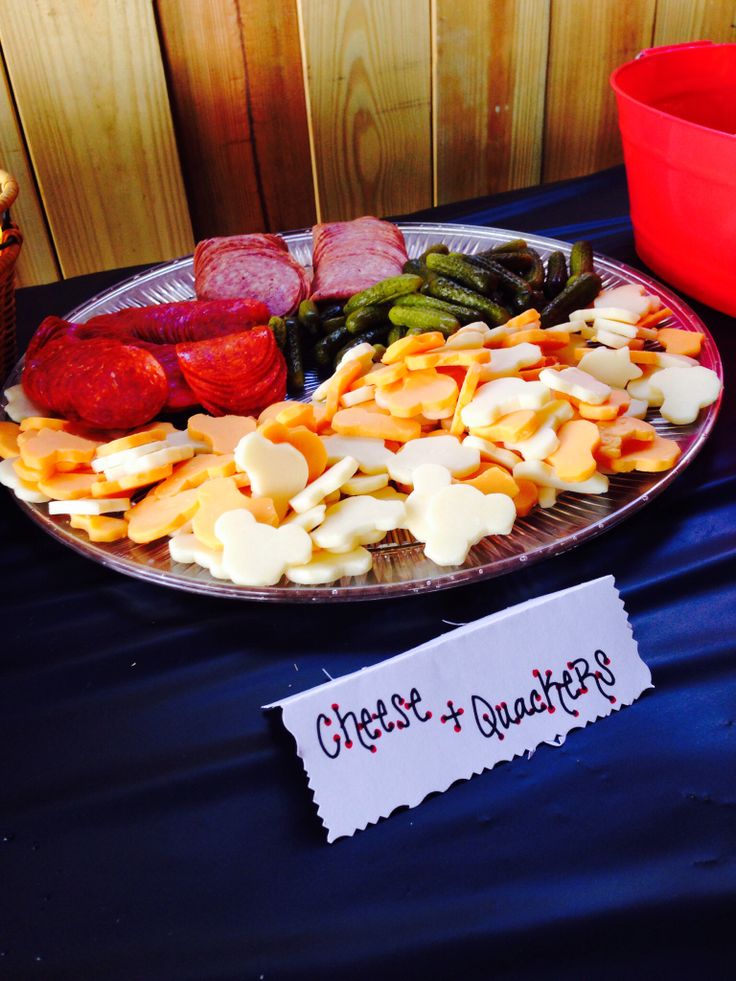 an assortment of cheese and meats on a platter next to a red bowl