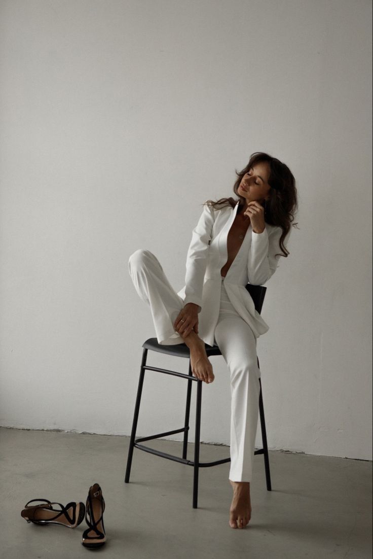 a woman sitting on top of a chair next to a pair of shoes and wearing a white suit