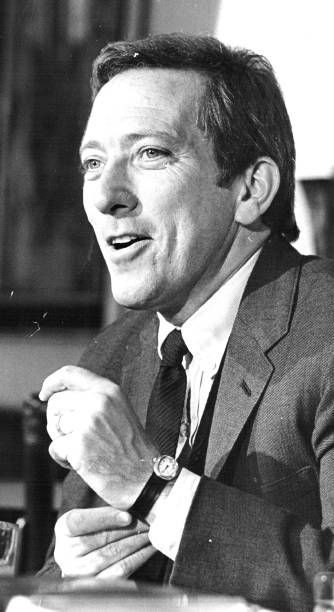 a black and white photo of a man in a suit sitting at a table talking