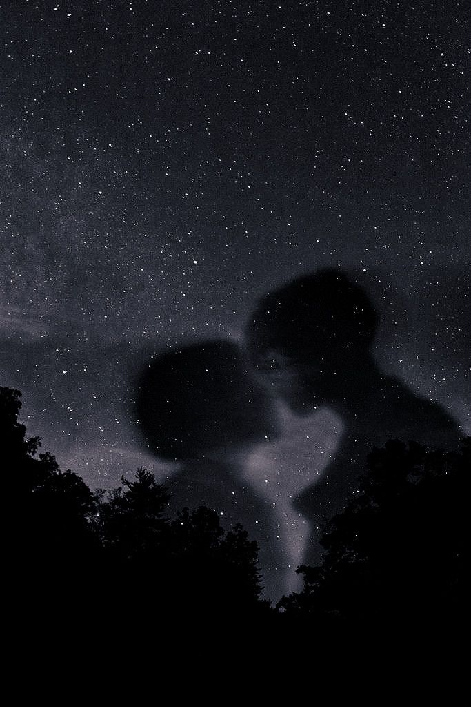 two people are kissing under the stars in the night sky, with trees silhouetted against them