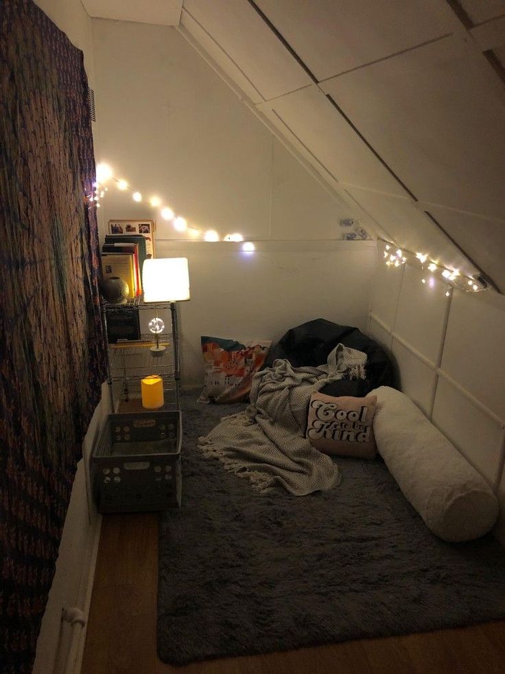 an attic bedroom with lights strung above the bed and pillows on the floor in front of it