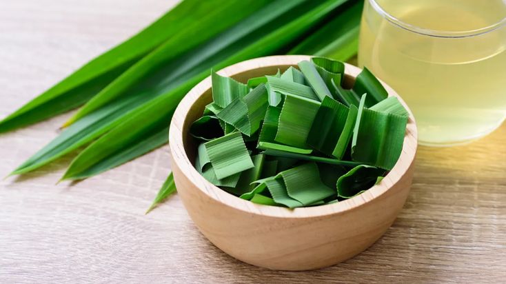 a wooden bowl filled with green leaves next to a glass of water