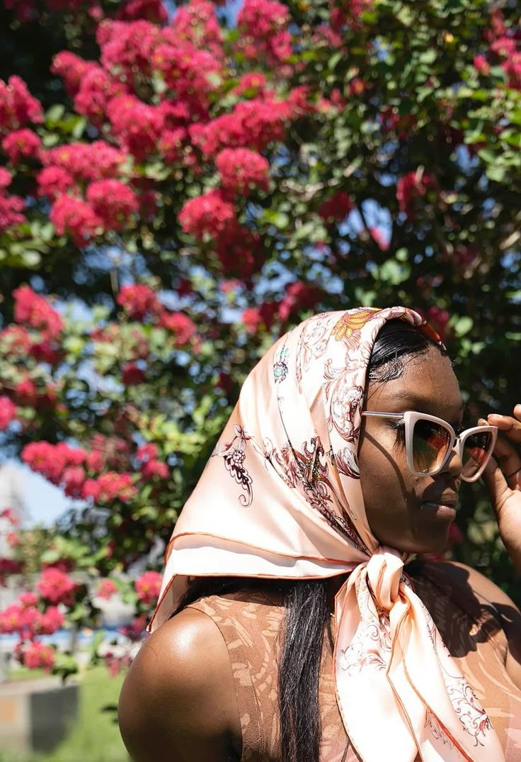 a woman wearing sunglasses and a scarf on her head is standing in front of a tree