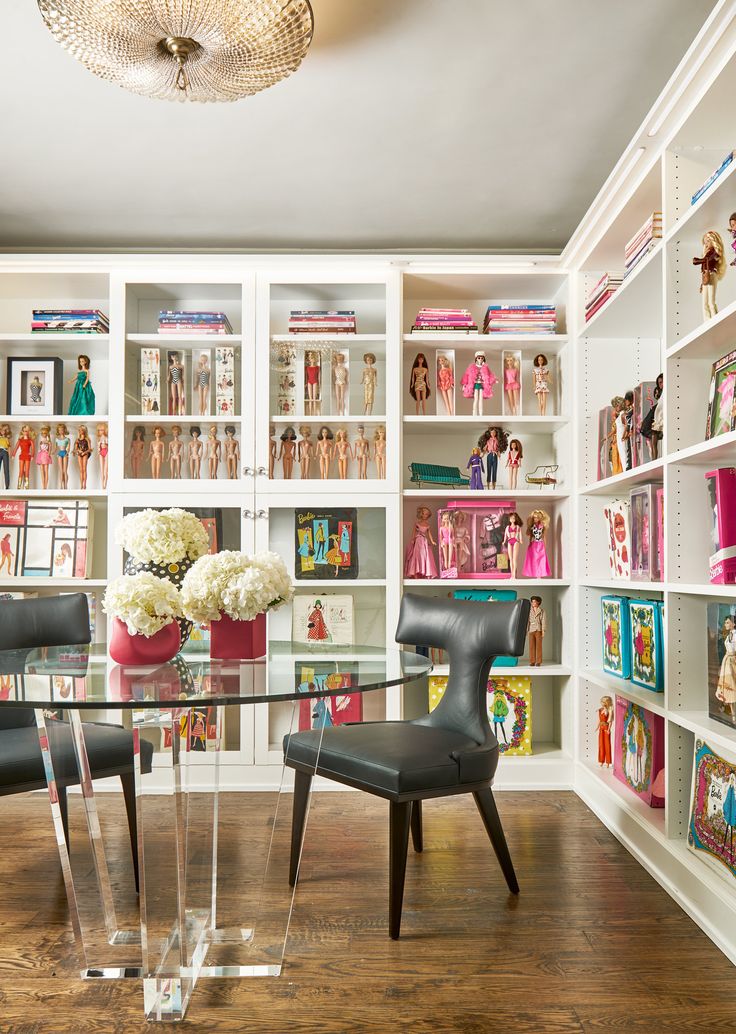 there is a glass table and chairs in this room with barbies on the shelves