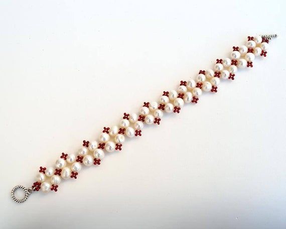 a red and white bracelet with pearls on it's end is shown in close up