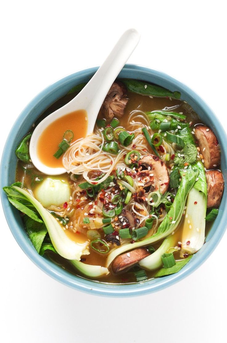 a blue bowl filled with noodles, meat and veggies next to a spoon