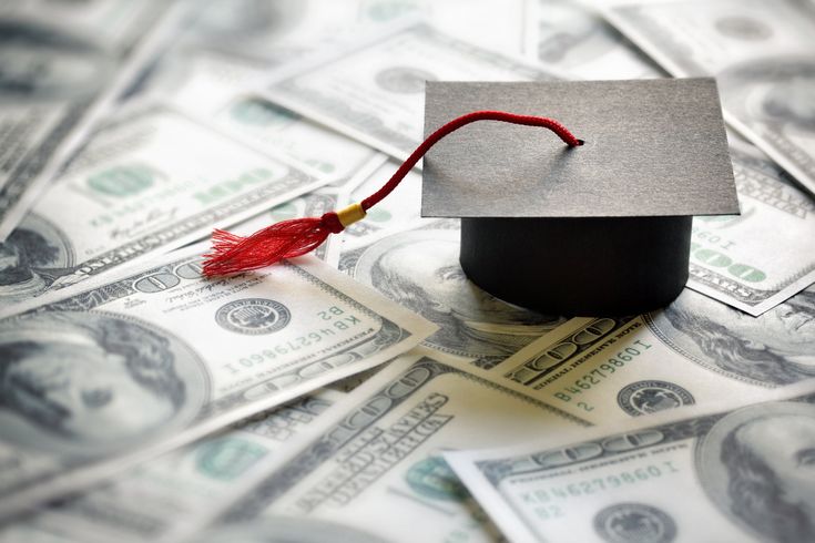 a graduation cap with a red tassel on top of hundred dollar bills in the foreground