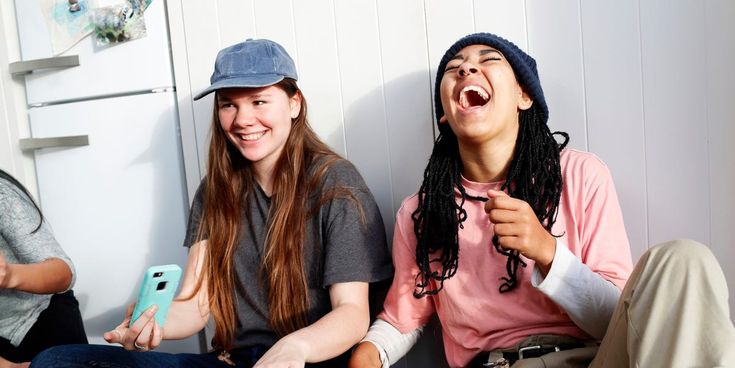 three young people sitting next to each other on the floor laughing and holding cell phones