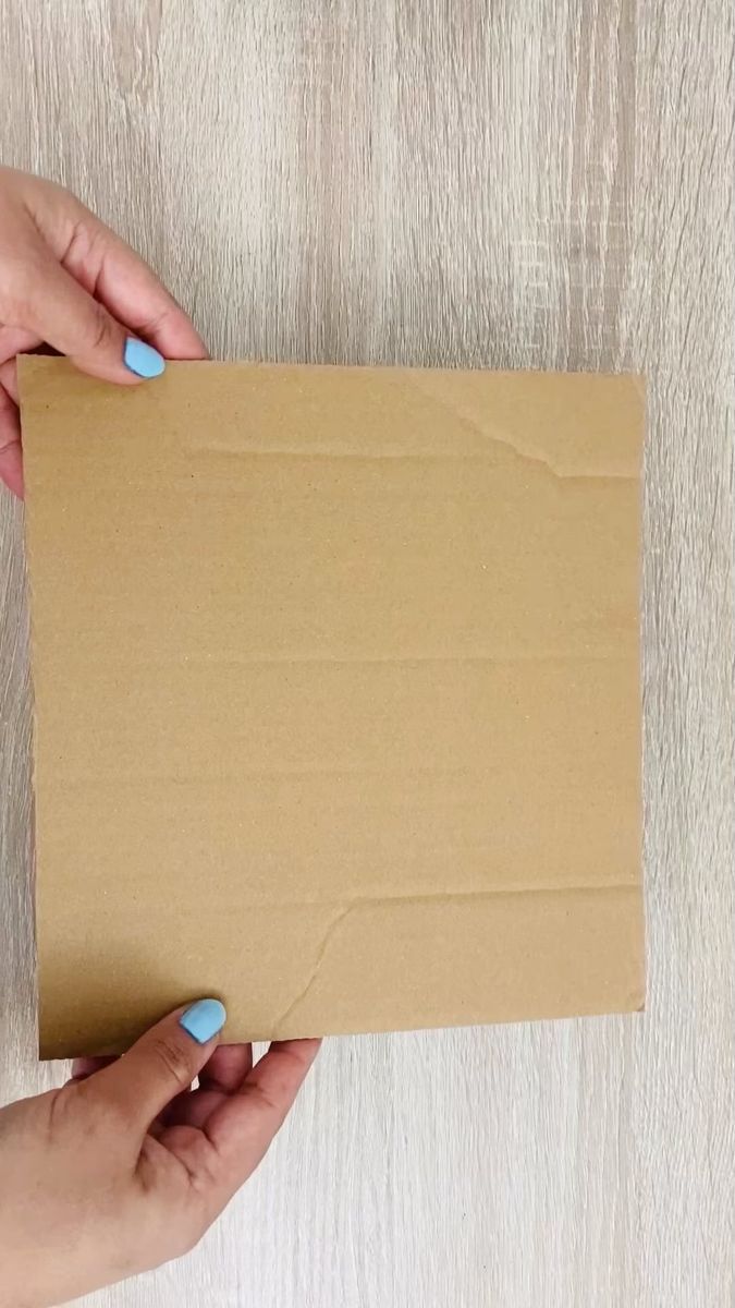 two hands holding a piece of cardboard on top of a wooden table with white wood flooring