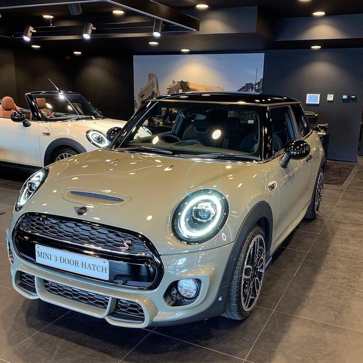 two mini coopers are on display in a showroom with people looking at them