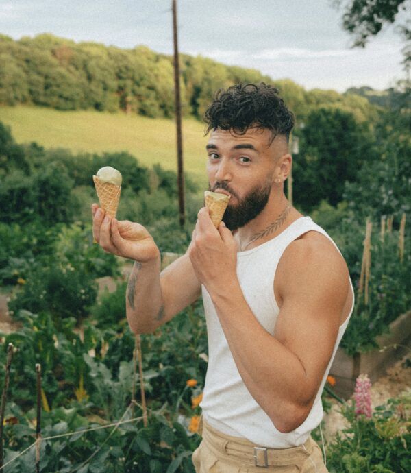 a man eating an ice cream cone in his hand while standing next to a garden