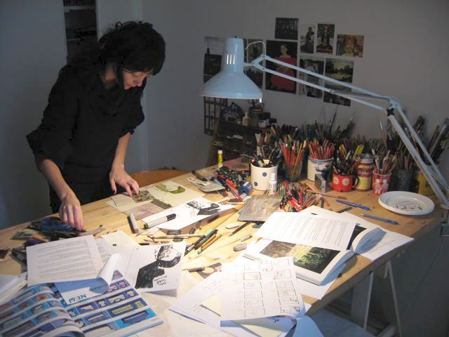 a man standing over a table with lots of papers on it and a lamp in the background