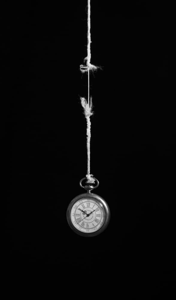 a clock hanging from a rope in the dark