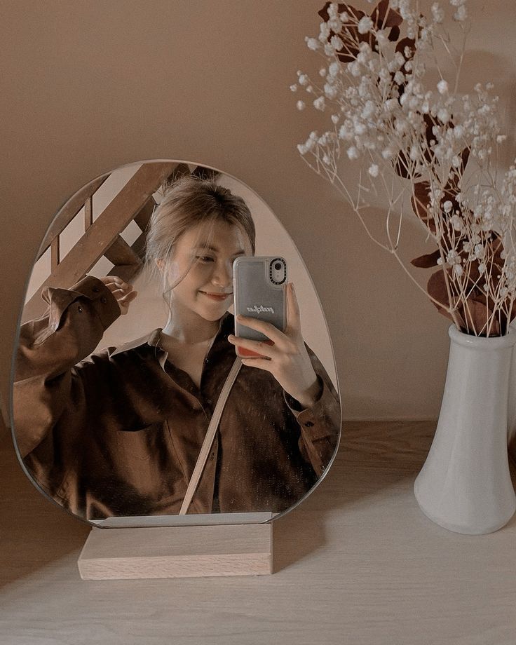 a woman taking a selfie with her cell phone in front of a round mirror