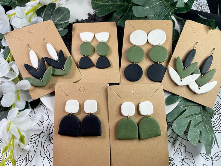 four pairs of earrings are shown in front of some white and green flowers on a table