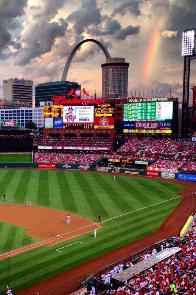 a baseball stadium filled with lots of people under a cloudy sky and a rainbow in the distance