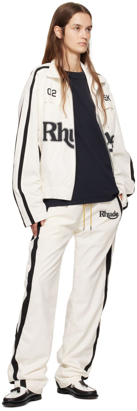 Polyester duck canvas track jacket. · Paneled construction · Funnel neck · Two-way zip closure · Text and logo printed at front · Welt and seam pockets · Elasticized hem · Dropped shoulders · Stripes at sleeves · Fully lined · Logo-engraved silver-tone hardware Supplier color: White/Black Cotton Outerwear With Logo And Crew Neck, Cotton Track Jacket With Logo Detail, Cotton Long Sleeve Track Jacket With Logo, Fall Streetwear Outerwear With Signature Stripes, White Sporty Outerwear With Logo Detail, Sporty White Outerwear With Logo Detail, Cotton Track Jacket With Zipper For Streetwear, Cotton Track Jacket With Embroidered Logo For Fall, Urban Cotton Track Jacket With Zipper