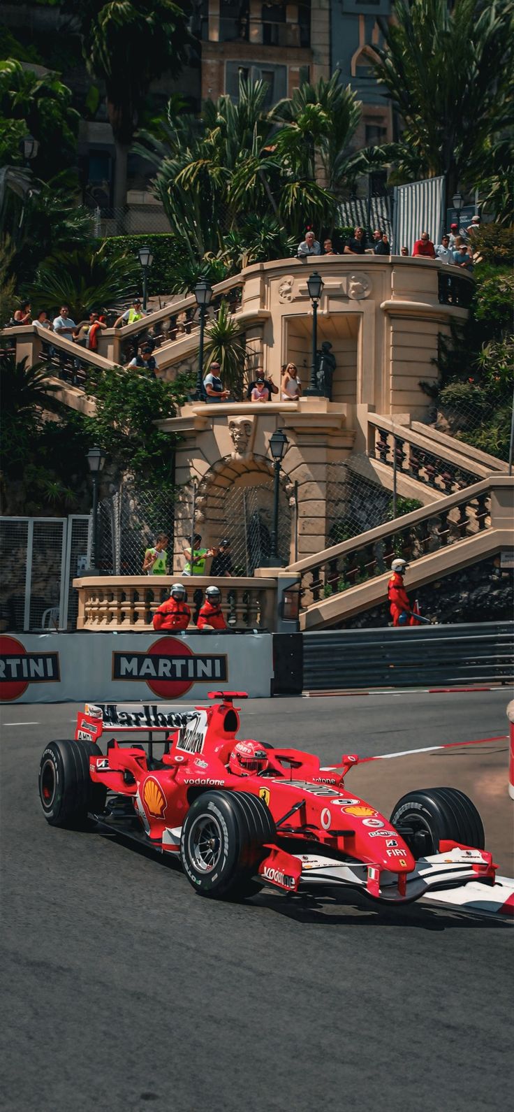 a man driving a red race car down a street next to a tall building with stairs