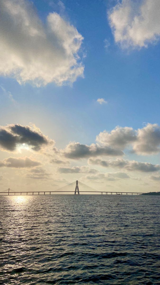 a large body of water under a cloudy blue sky with a light house in the distance