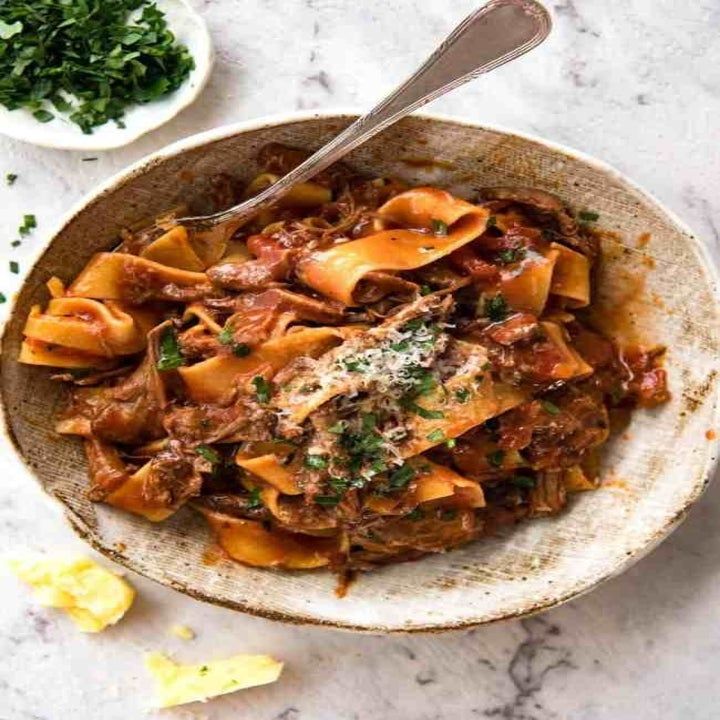 a bowl full of pasta with meat and parmesan cheese on top, ready to be eaten