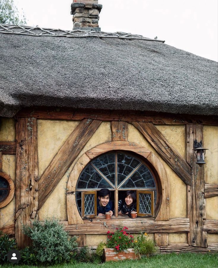 two people are looking out the window of a hobbot style house with thatched roof