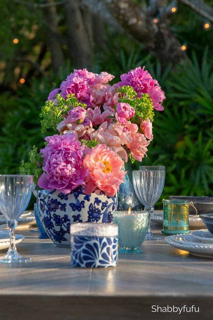 pink flowers are in a blue and white vase on a table with wine glasses, candles and plates