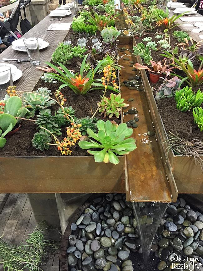 a long table with lots of plants and water running down the center, surrounded by people sitting at tables