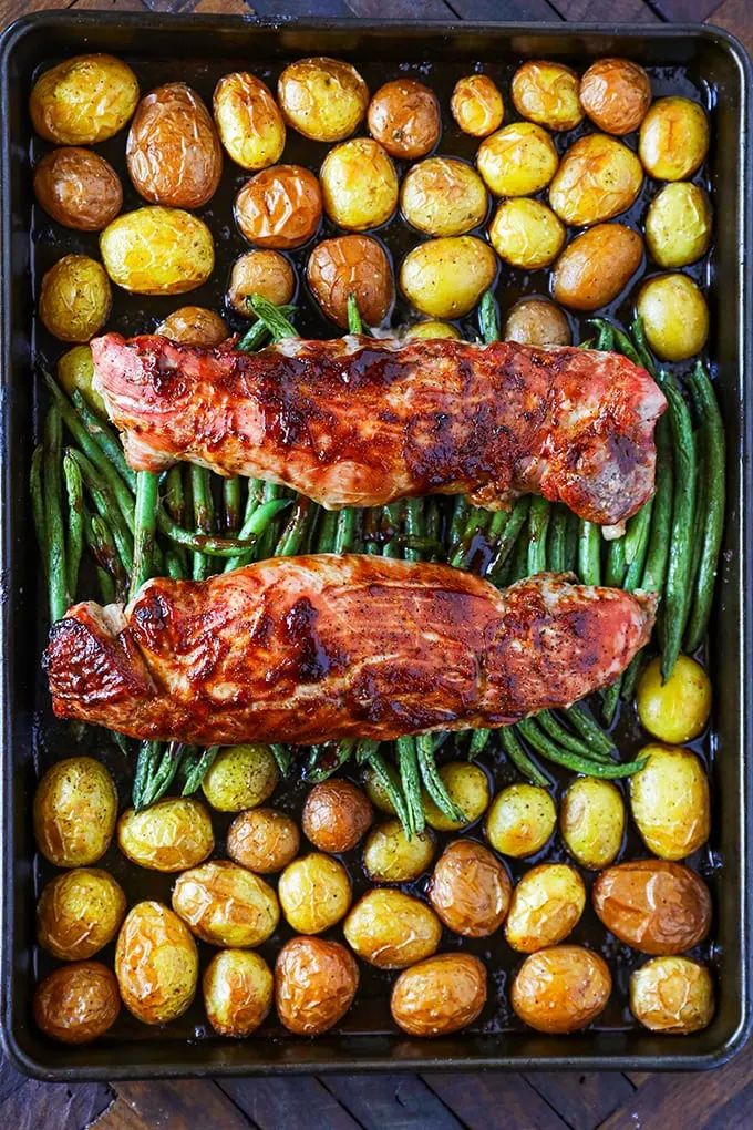 two porks and green beans in a roasting pan with potatoes on the side