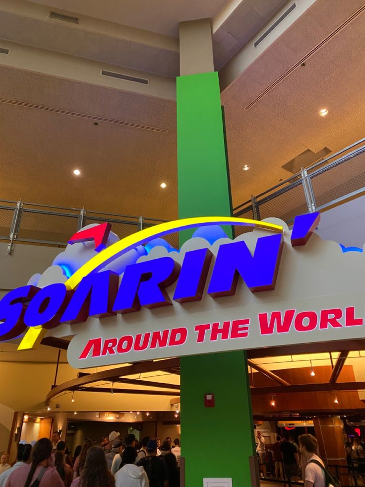 people are standing in front of the sign for soarn around the world at an indoor mall