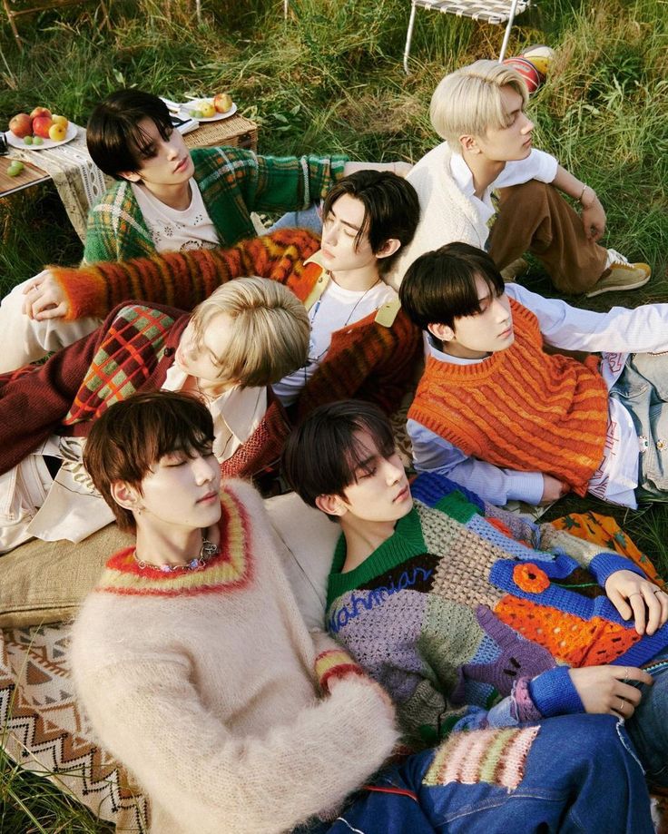 group of young men sitting on the grass with food and drinks in their hands, all wearing sweaters