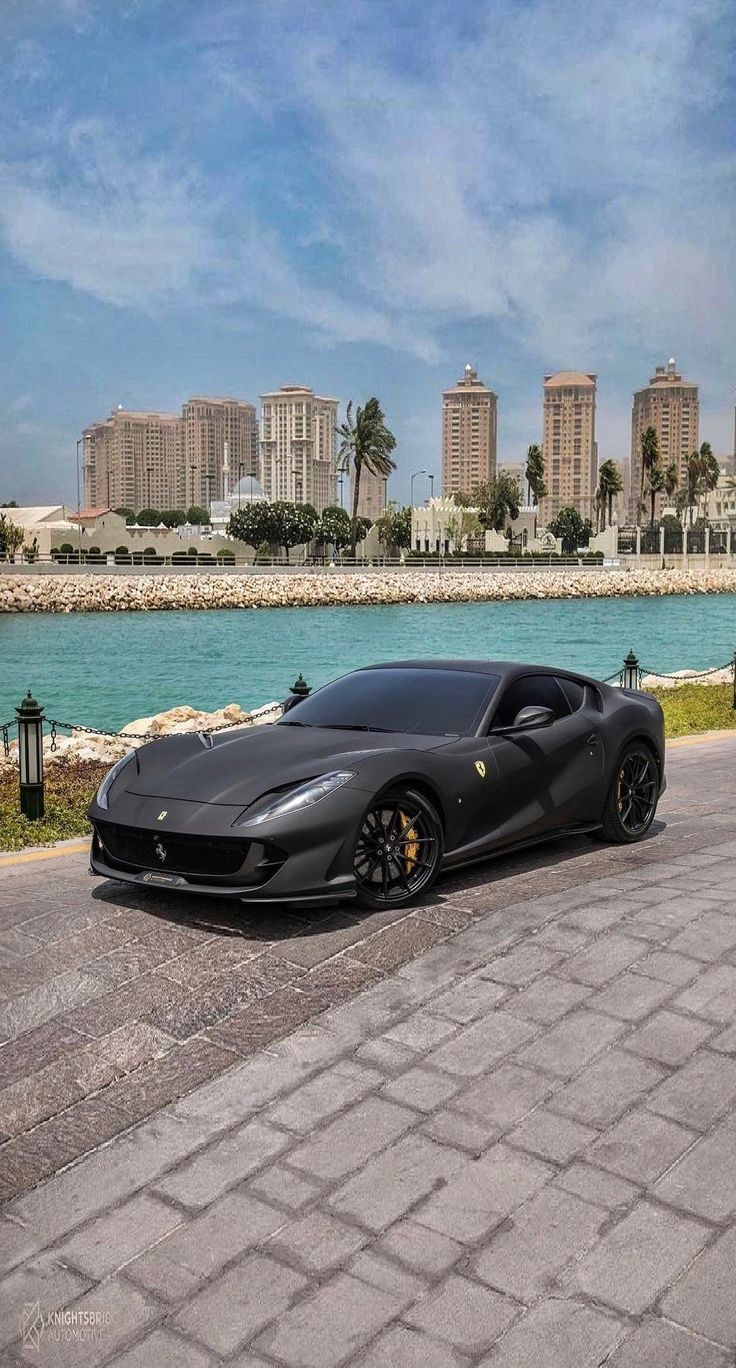 a black sports car parked in front of a body of water with buildings in the background