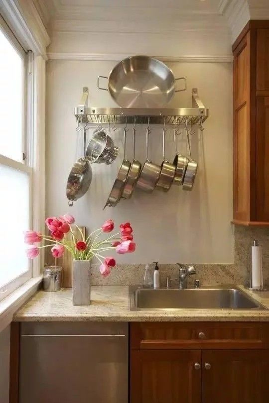 pots and pans are hanging on the wall above the sink in this small kitchen