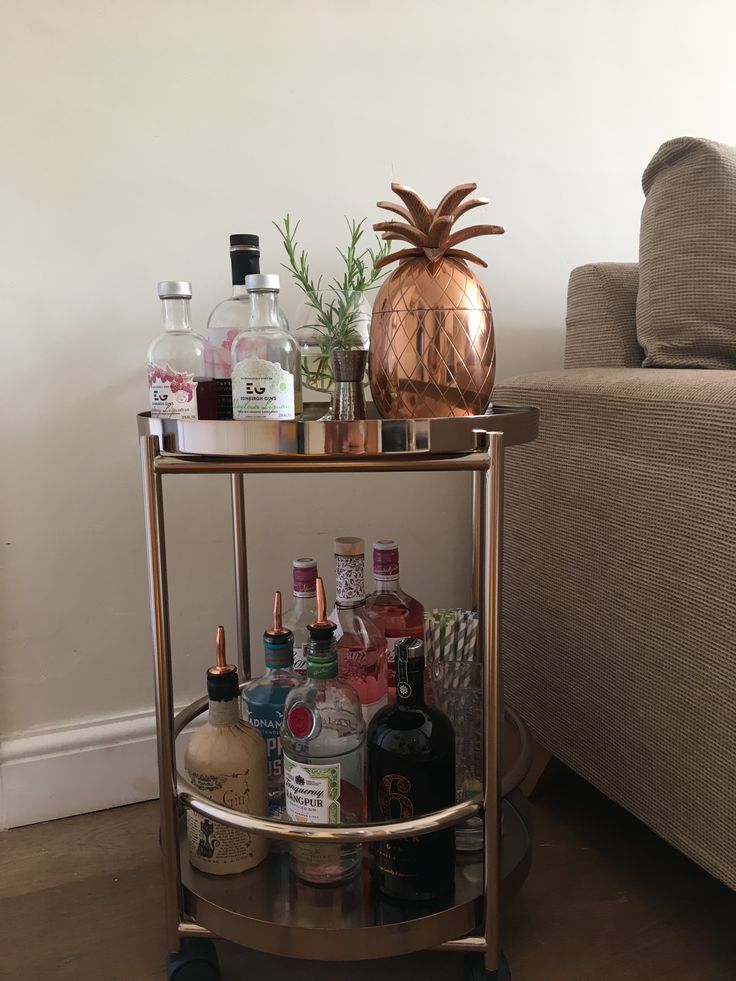 a gold bar cart with liquor bottles on it and a pineapple vase in the corner