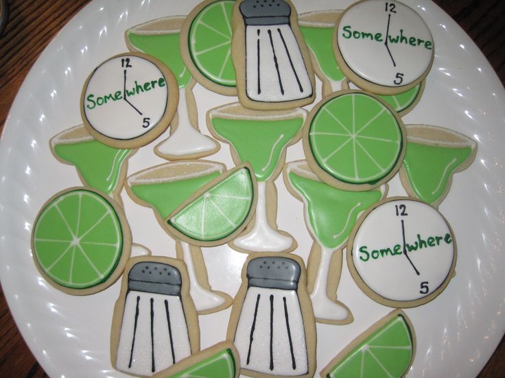 decorated cookies on a white plate with limes and cocktail glasses in the shape of cutouts