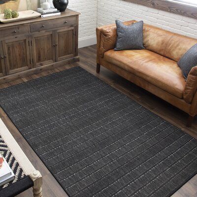 a living room with a brown leather couch and black area rug in front of a window