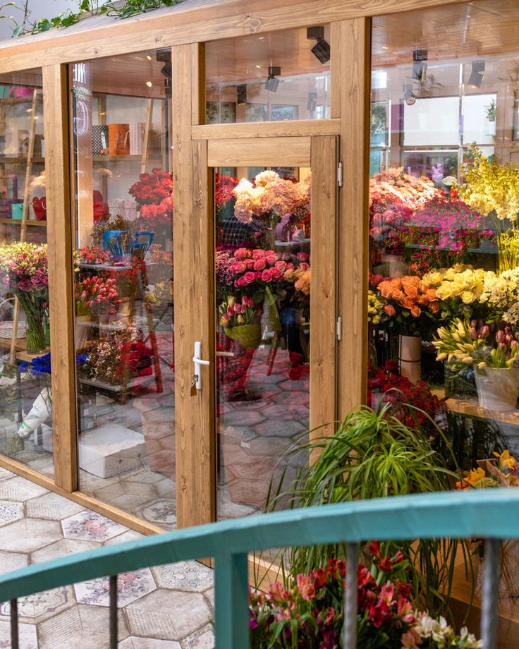 a flower shop filled with lots of different types of flowers in glass walls and doors