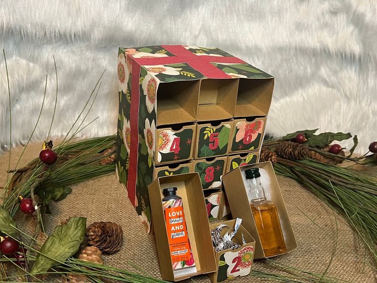 an open box with two bottles and pine cones on the ground next to christmas decorations